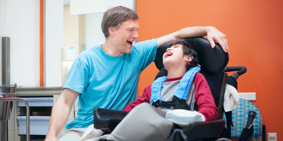 A carer having a laugh with a child who is in a wheelchair.