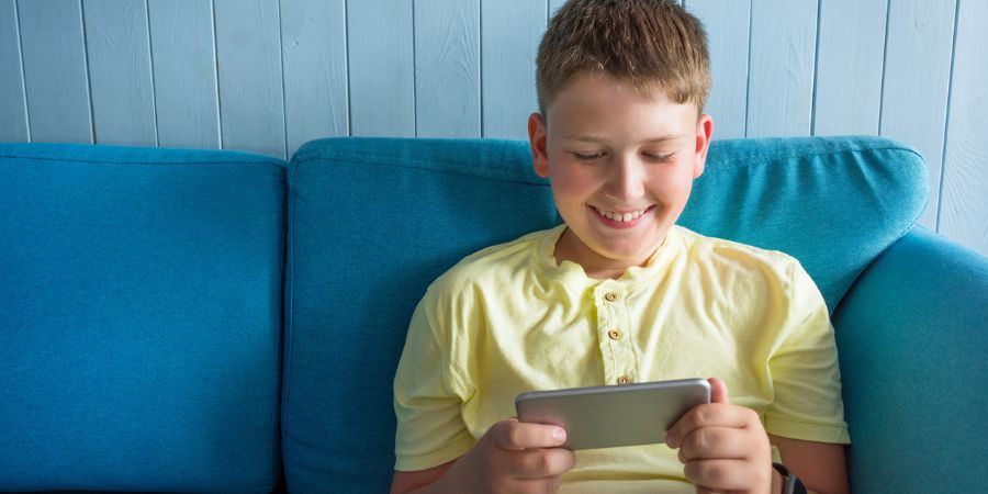 A smiling boy sitting on the sofa looking at his mobile phone.