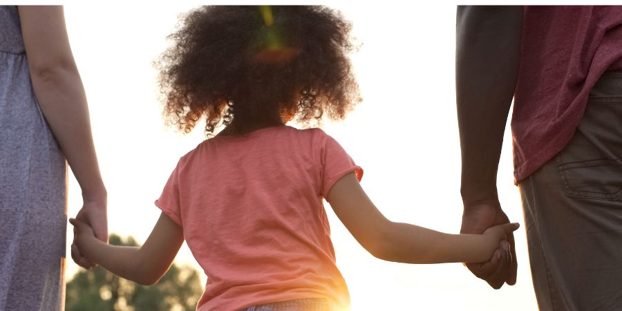 A child in between her parents, holding their hands.