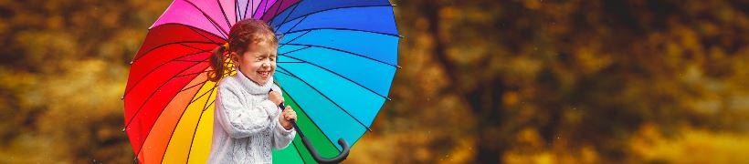 A girl jumping in a puddle while holding an umbrella.