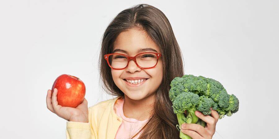 A young girl with an apple and broccoli.