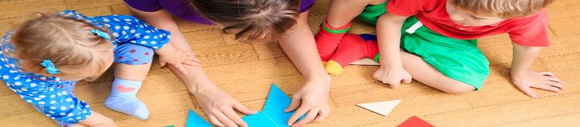 A carer and children playing with cardboard shapes on the floor.