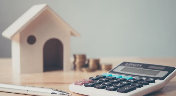 Calculator and coins next to a toy house.