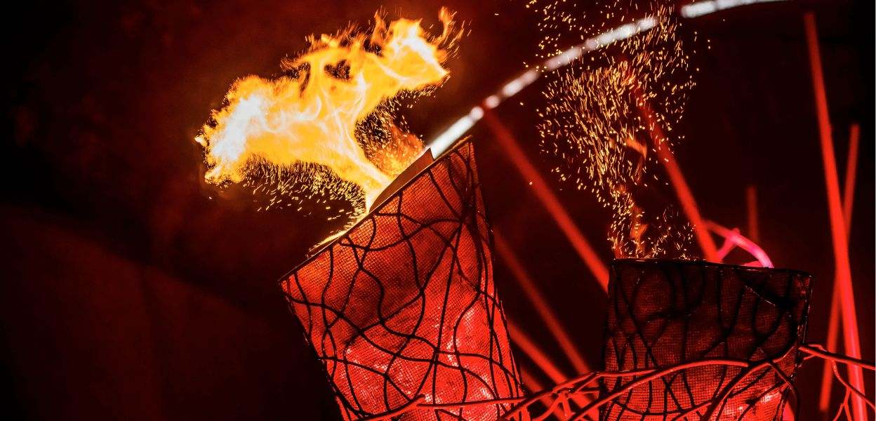A flame in front of a cracked black metal  sculpture with red glowing lines and sparks flying through the air.