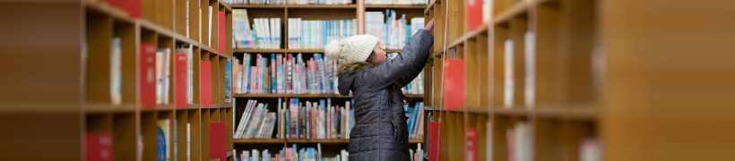 A child reaching for a book in the library.