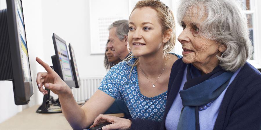 An elderly lady being shown how to use a computer.