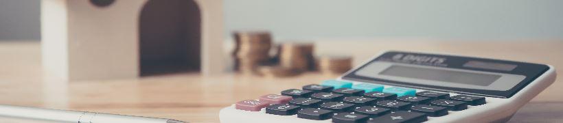 A calculator on a desk with piles of coins in the background.