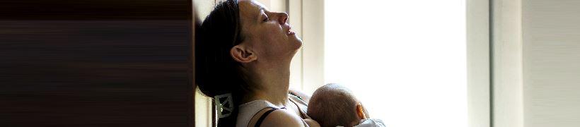 A stressed mother holding a baby, her head resting back against the wall.