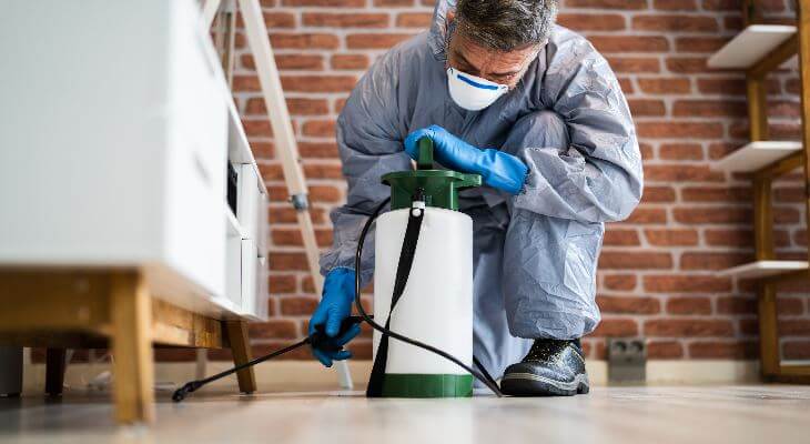 A pest controller spraying underneath a table.