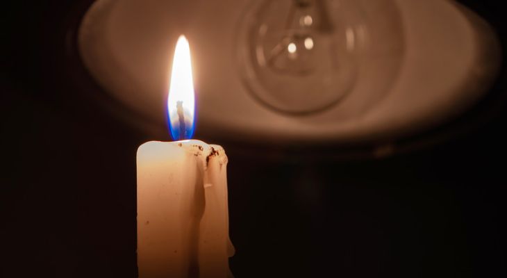 A lit candle in front of a lightbulb with no power.