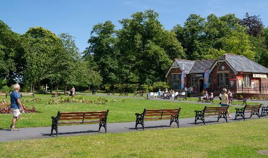 Queen&#039;s park. People walking round the park and a row of park benches