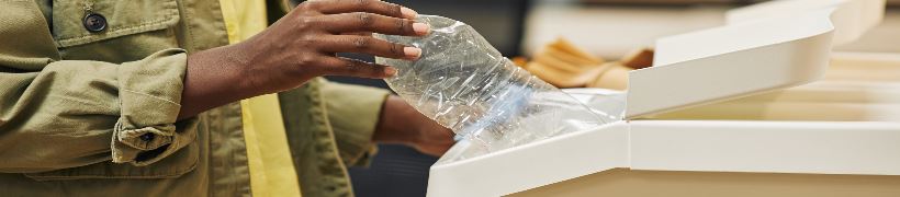 Close up of a hand dropping an empty plastic bottle into a recycling bin.