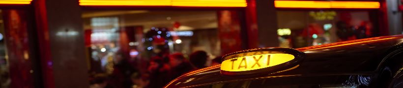 An illuminated taxi sign on top of a black cab.