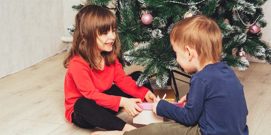 2 children playing beside a Christmas tree.