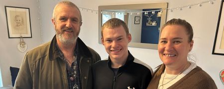 3 people stand together smiling for a photo indoors.