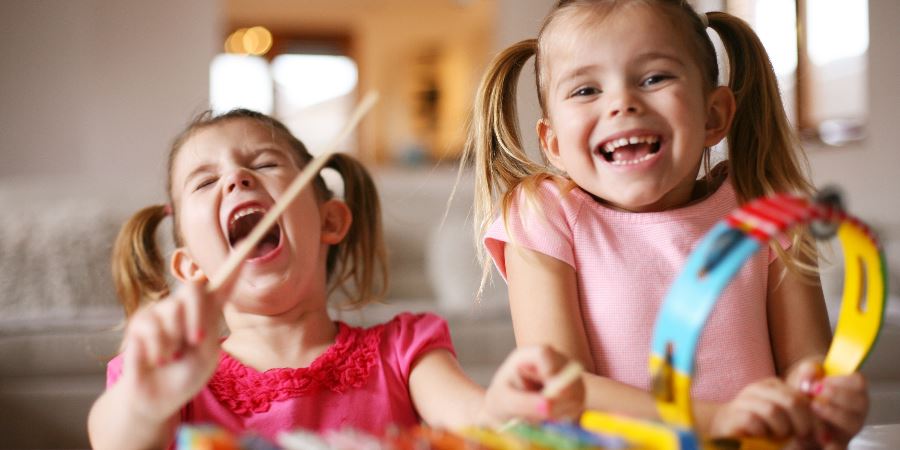 2 young girls playing with tambourines and laughing.